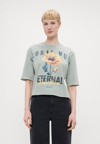Mintgrønn kortermet t-skjorte med blomstertrykk i gult og blått, med teksten "ETERNAL Sunshine" i metallisk gull og svart.