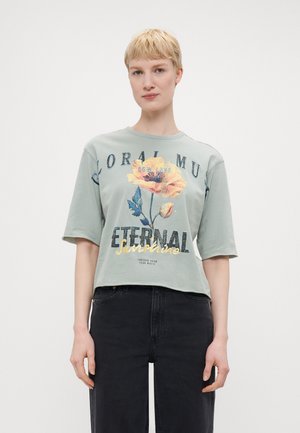 T-shirt cropped vert menthe avec imprimé floral jaune et bleu, comportant le texte "Eternal Sunshine" en doré métallisé et noir.