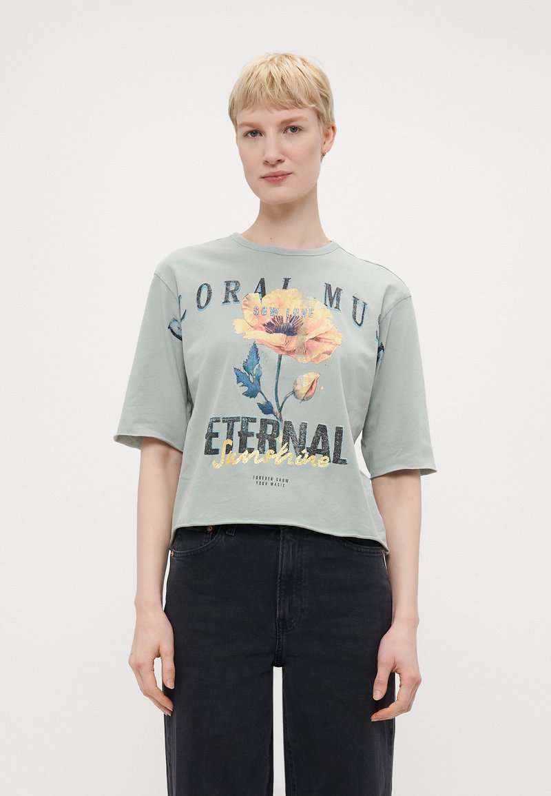 Mintgrønn kortermet t-skjorte med blomstertrykk i gult og blått, med teksten "ETERNAL Sunshine" i metallisk gull og svart.