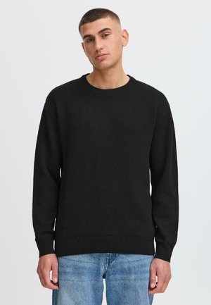 Black knit sweater with a round neckline and long sleeves. Features ribbed accents at cuffs and hem, worn over blue distressed jeans.