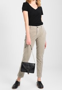 Maglietta nera a v-neck, pantaloni aderenti beige chiaro e scarpe di pelle nere. Piccola borsa nera con accessori dorati, tracolla a catena.