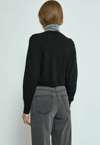 Schwarzer, kurz geschnittener Pullover mit puffigen Ärmeln, kombiniert mit hochgeschnittenen grauen Jeans, die zwei Gesäßtaschen und eine leichte Textur besitzen.