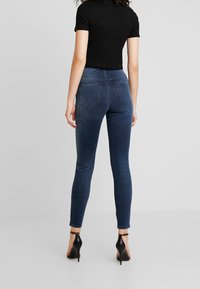 Úzké modré džíny s jemným elastickým materiálem, vybavené dvěma zadními kapsami a středně vysokým pasem, doplněné černým přiléhavým tričkem s krátkým rukávem.