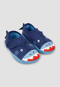 Des chaussures sur le thème des requins bleus présentent un dessus en tissu doux, une large sangle Velcro et un visage de requin coloré sur les orteils avec des accents de dents rouges.