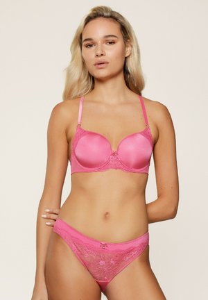 Roze gewatteerde bh met kantafwerking, verstelbare bandjes en een decoratieve strik in het midden. Bijpassende sheer lace strings met ingrijpende patronen.