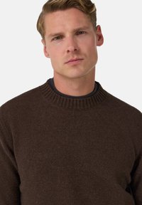 Hnědý pletený svetr s žebrovaným kulatým výstřihem, vyrobený z jemné látky, s jemnou texturou a volným střihem.