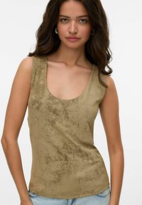 Top khaki senza maniche con scollatura tonda, texture liscia e delicato motivo irregolare. Abbinato a jeans in denim azzurri chiari.