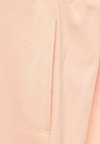Tissu de jogger en coton rose pâle avec une poche latérale dotée d'une couture. La texture est lisse, avec un léger stretch.