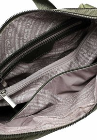 Rohelise lõuendiga koti sisemus mitme sahtliga, millel on sile lilla vooder korduva tekstimustriga, hõbedaste tõmblukkude ja õmblustega.