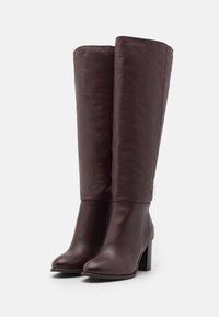 Bottes en cuir bourgogne montantes avec une texture lisse, bout rond et un talon bloc robuste, arborant un design élégant et minimaliste.