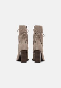 Bottines en suède beige avec un bout rond, un haut talon en bois et un détail de lacet noué à l'arrière avec une fermeture éclair.