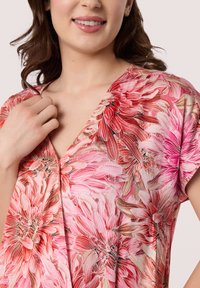 Bloes met bloemenprint, voorzien van levendige roze en koraalroze bloemen op een lichtgewicht stof. V-halsontwerp met korte mouwen en subtiele textuurdetails.
