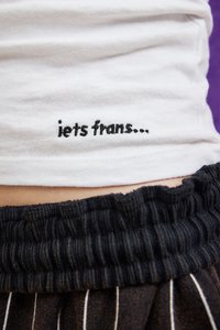 White t-shirt with black embroidered text reading "iets frans..." at the hem, paired with black ribbed waistband of striped pants.