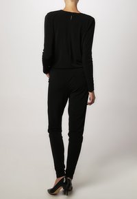 Mono negro con mangas largas, forma ajustada y un pequeño detalle de ojal en la parte posterior. Tela suave y elástica combinada con zapatos de tacón alto.
