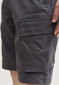 Shorts cargo gris en coton avec poches latérales. Présente des détails cousus et une étiquette en relief sur la poche.