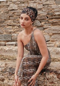 Haljina leopard uzorka s dizajnom na jedno rame, u zemljanim tonovima i mekane teksture. Stilizirana s odgovarajućom trakom za glavu i zlatnim nakitom.