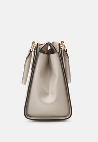 Beżowa skórzana torebka o zorganizowanej, ale miękkiej formie, z złotymi elementami, górnym zamkiem błyskawicznym oraz kontrastowym ciemnym wykończeniem wzdłuż krawędzi.