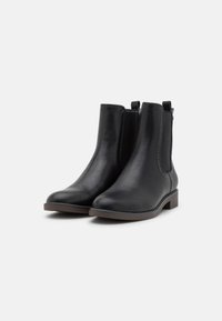 Botas de tobillo de cuero negro con paneles laterales elásticos, un tacón bajo apilado y costuras decorativas a lo largo de las costuras. Textura suave.