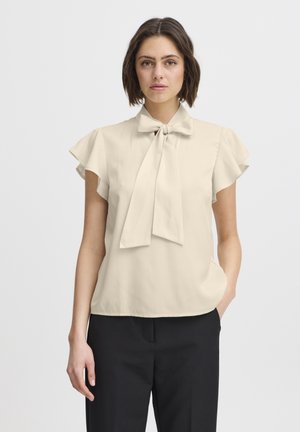 Beige blouse with a bow tie neckline, short ruffled sleeves, smooth texture, and a relaxed fit. Paired with dark, tailored pants.