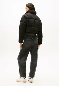 Zwart cropped puffer jack met een hoge kraag, grote gequilte secties en een gladde textuur, gecombineerd met hoge taille donkere spijkerbroek.