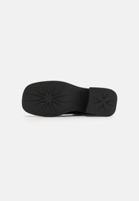 Svart såle med teksturerte gripe mønstre, med et lett hevet, glatt hælområde og en buet form for ergonomisk design.