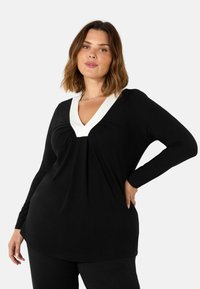 Musta pitkähihaine paita, jossa on syvä V-kaula-aukko ja kontrastivärinen valkoinen kaulus. Pehmeä kangas, jossa on rypytystietoa rinnassa, lisäämään muotoa.