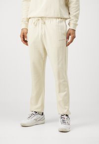 Krämfärgade sweatpants med elastisk midja och snörning, sidofickor och en liten logotyp på vänster lår. Mjuk textur.