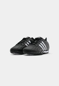 Black athletic shoes featuring a smooth leather upper, white three-stripe design, lace closure, and textured rubber sole.