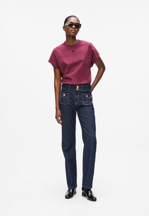 Camiseta corta de manga en burdeos, jeans de mezclilla oscuros de cintura alta con herrajes dorados, combinada con gafas de sol negras y botines.