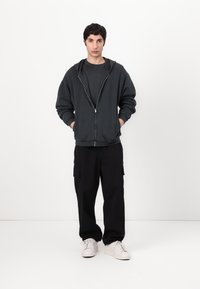 Dark gray zip-up hoodie over a matching gray T-shirt, paired with black cargo pants and white sneakers. Simple, relaxed fit, and no patterns.