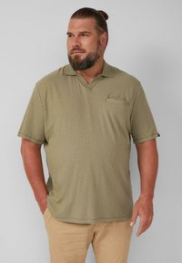 Olijfgroene polo met korte mouwen, van ribbelstof, met een V-hals en een borstzak aan de linkerkant, gecombineerd met beige broek.