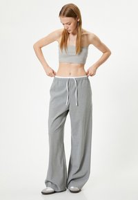 Pantalones de pierna ancha a rayas en gris claro con cintura elástica y cordón blanco, combinados con un top gris sin mangas. Textura suave.