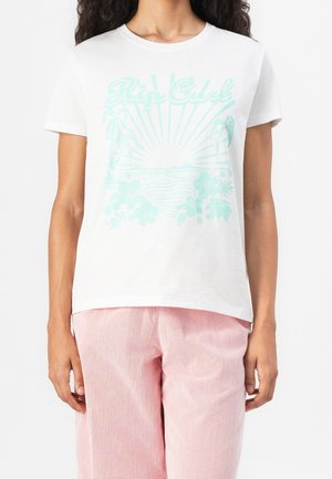 Person wearing white T-shirt with light blue tropical sunset graphic and pink pants against a white background.