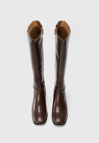 Ein Paar hohe, braune Lederstiefel mit viereckigen Spitzen und seitlichen Reißverschlüssen, auf einem schlichten weißen Hintergrund aufrecht präsentiert.