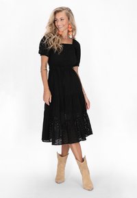 Rochie neagră, până la genunchi, cu manșete scurte și puff, model cu perforații, talie ajustată și fusta în straturi. Asortată cu cizme de gleznă bej, perforate.