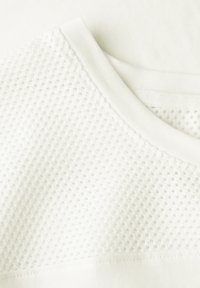 T-shirt de sport blanc avec un panneau en maille texturée et un tissu lisse. Encolure ronde avec une bordure côtelée. Matière douce et légère.