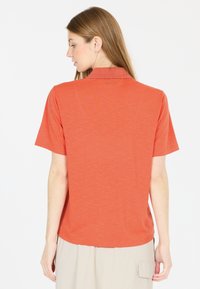 Kortärmad orange polo med krage, tillverkad av ett texturerat tyg och med avslappnad passform, bärs tillsammans med beige byxor.