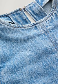Denimkangas vaalean sinisen pesun kanssa, jossa on pyöreä kaula-aukko ja pieni leikkuukohta selässä. Kontrastitikkaus on näkyvissä.