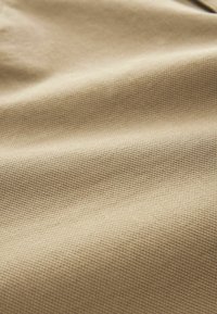 Tissu beige texturé avec un motif tissé fin. Le matériau semble solide et durable, adapté pour les vêtements ou les accessoires.