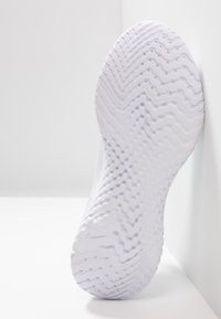 Weiße Sport-Schuhsohle mit strukturiertem Wellenmuster und runden Aussparungen, leicht schräg vor hellem Hintergrund.