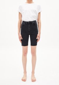Shorts de mezclilla negros de cintura alta con dobladillo deshilachado, corte recto y diseño de cinco bolsillos, combinados con una camiseta blanca de corte holgado.