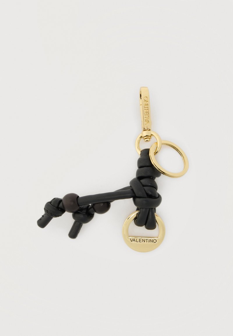 Μαύρο δερμάτινο μπρελόκ με κόμπους και χρυσούς κρίκους, ο ένας χαραγμένος με τη λέξη «Valentino», σε απλό ανοιχτό φόντο.