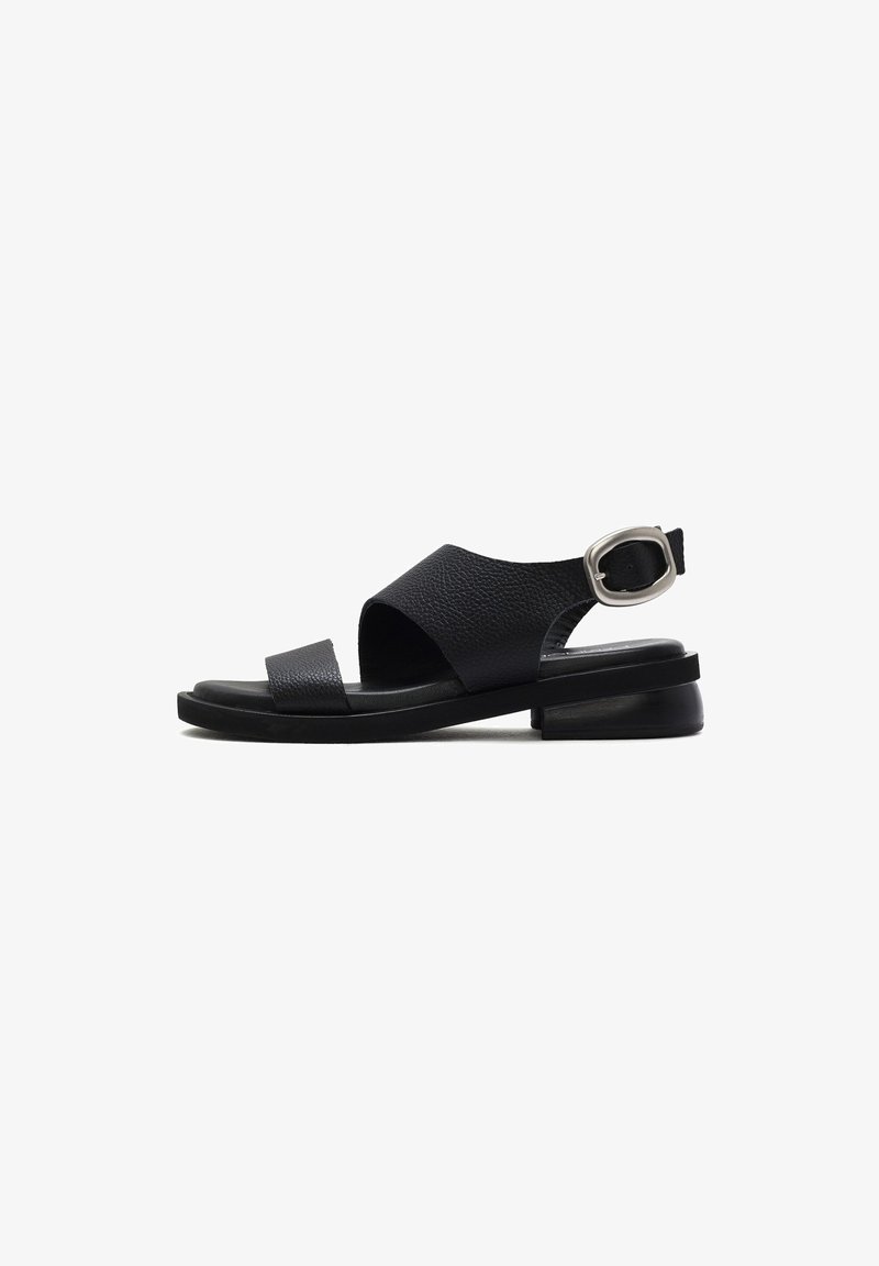 Black leather sandal with a textured upper, open toe, and ankle strap featuring a silver buckle. Low, flat sole for comfort.