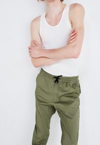 Vit ärmlös tanktop som bärs med byxor i olivgrön med elastisk midja. Byxorna har dragsko, sidofickor och en slät yta.