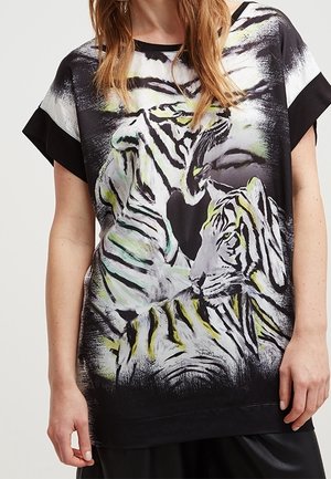 Zwart topje met korte mouwen, afgebeeld met een grote, artistieke tijgerprint in witte en groene tinten. Soepele stof met een losse pasvorm en een afgeronde halslijn.