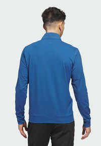 Plava polo majica dugih rukava sa strukturiranim ovratnikom, glatkom teksturom i krojem koji pristaje tijelu. Ima pojas na donjem rubu i duge rukave.