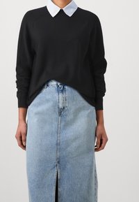 Schwarzer Pullover mit weißem Kragen, kombiniert mit einem Jeansrock mit Fronteinschnitt und hellblauer Waschung. Weiche Textur und lockere Passform.