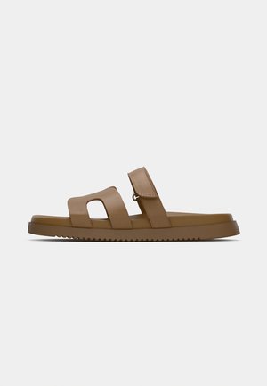 Bruna sandaler med två breda remmar, ett urtagningdesign och en texturerad sula. Tillverkade av ett mjukt material med en platt, vadderad fotbädd.
