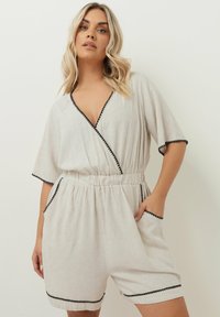 Ljusbeige linnejump suit med korta ärmar, elastisk midja och svart kant längs halsringningen och fickorna. Har en avslappnad passform.