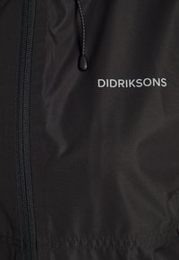 Czarna wodoodporna kurtka o fakturowanym wykończeniu, z przednim zamkiem błyskawicznym, regulowanym kapturem ze ściągaczem oraz białym logo „DIDRIKSONS”.